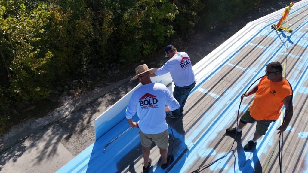 Bold Roofing crew spraying acrylic basecoat on a commercial metal roof in southwest Missouri
